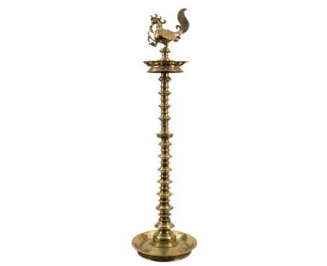 An Indian Deccan brass oil lamp: with cockerel finial and reservoir below, on a knopped turned column with circular flange ba