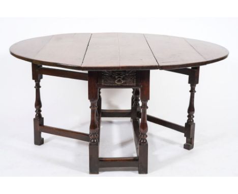 An 18th century oak oval gateleg table:, with a hinged top, the frieze fitted with a drawer with applied 17th century panel d