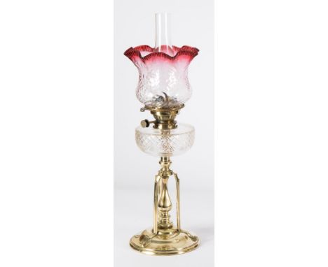 An Arts & Crafts influence brass oil lamp: with Hicks No 2 Lever wick holder, having a clear glass circular reservoir, raised