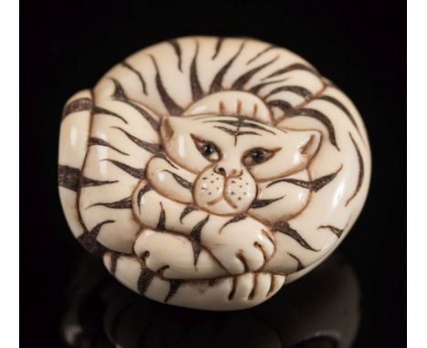 A Japanese carved ivory netsuke of a tiger: curled up, with inset eyes, having stained stripes, signed,  4cm. diameter.