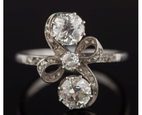 A platinum and diamond ribbon cross-over cluster ring: the two principal round old brilliant-cut diamonds each approximately 