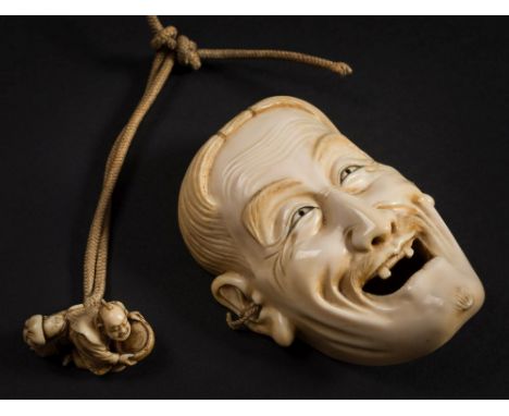 A Japanese carved ivory miniature mask: of a laughing man with open mouth and only two teeth, signed, 11cm. high with a cord 