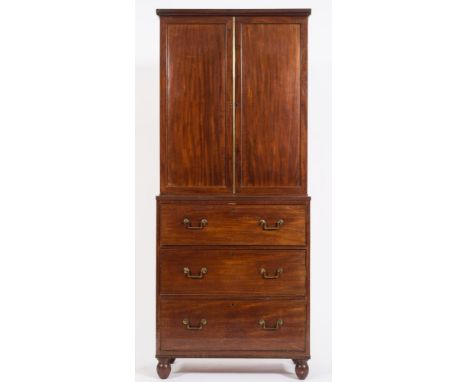 An early 19th Century mahogany cabinet on chest:, the upper part with fixed shelves enclosed by a pair of moulded panel doors
