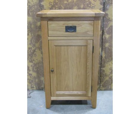 A contemporary oak free standing side cupboard partially enclosed by a panelled door beneath a frieze drawer, 101cm high x 60