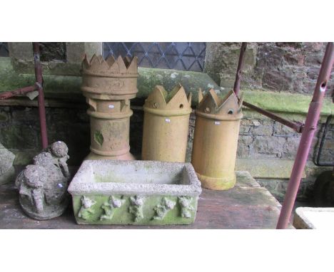 A weathered rectangular cast stone trough with repeating cherub detail, together with three buff coloured crown top chimney p