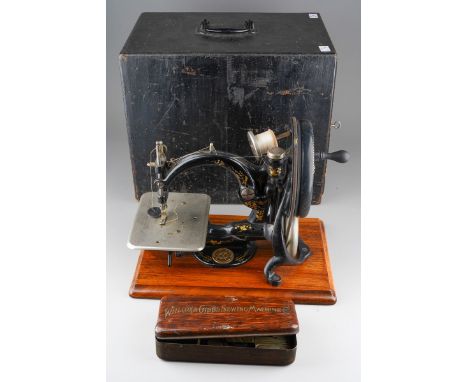 An early 20th century Willcox &amp; Gibbs table top manual sewing machine with arched arm, mounted on a rectangular walnut ba