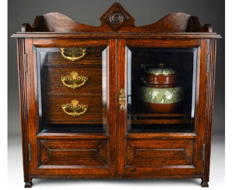 An Edwardian oak smokers cabinet, raised back above bevel edge glazed double doors enclosing a shelf with two pipe rests and 