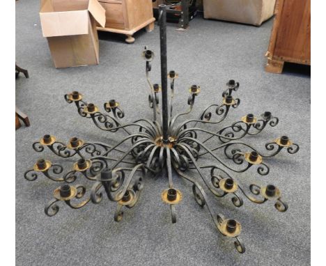 A wrought iron twenty four light chandelier, the scroll form branches fitted to a turned central column, 120 cm diameter x 70