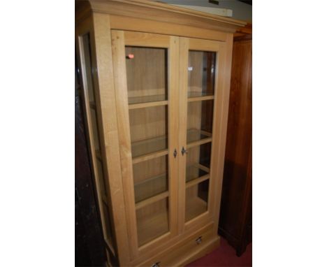 A good quality contemporary joined light oak double door glazed freestanding display cabinet, having single long lower drawer