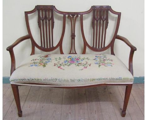 A late 19c Hepplewhite style two seater sofa with swag carved shield shaped back, having open arms with leaf carved terminals