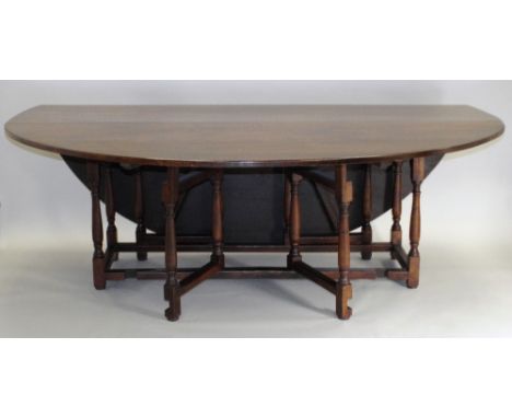 A 20th century reproduction oak double gate-leg dining table, the oval top on slender baluster supports united by plain side 