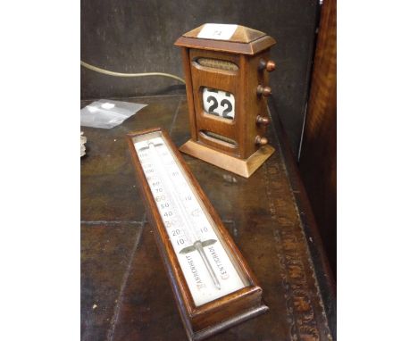 AN OAK CASED ADJUSTABLE DESK CALENDAR and a wall hung thermometer 