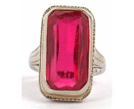 An 18kt synthetic ruby ring, the rectangular radiant synthetic ruby, collet mounted with millegrain border and deep pierced g