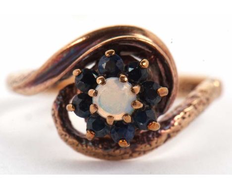 A 9ct sapphire and opal ring, the central round opal cabochon, surrounded by small round sapphires, in a spiralled mount and 