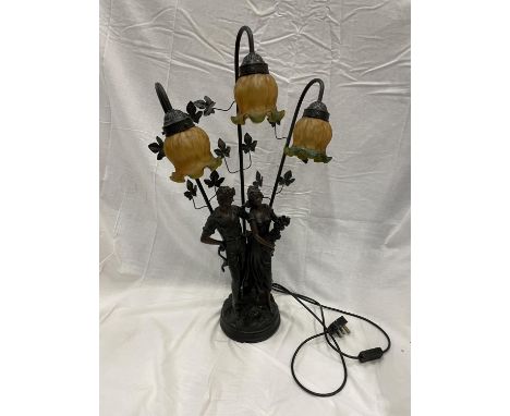 AN ART DECO STYLE LAMP WITH COURTING COUPLE DECORATION AND THREE LIGHTS WITH AMBER AND GREEN FLUTED SHADES 75CM HIGH 