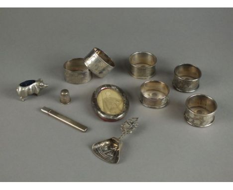 Four silver napkin rings, together with two silver thimbles, a continental white metal caddy spoon, a silver decanter label '