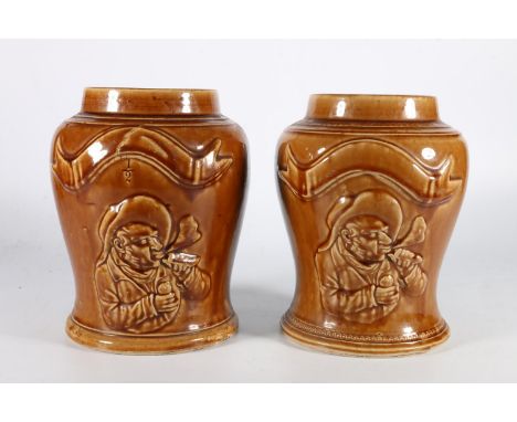 Pair of pottery tobacco jars in brown rocking style glaze with portrait of a gentleman smoking a pipe, 21cm tall.&nbsp; 
