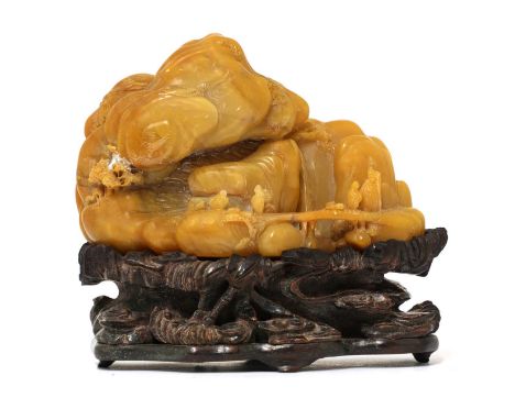 A Chinese soapstone boulder carving,of literati and attendants in a rocky landscape with buildings and streams, the stone of 