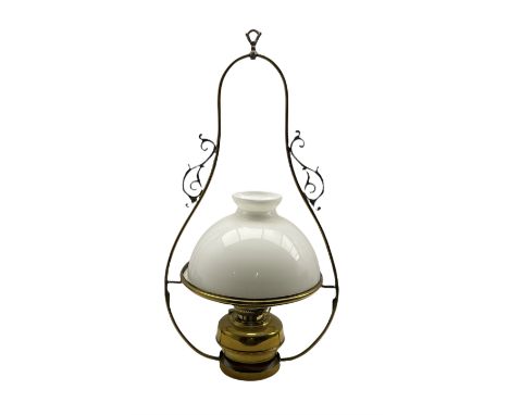 Victorian brass hanging oil lamp having a brass oil reservoir, white opaque glass domed shade and outer scroll pendant hangin