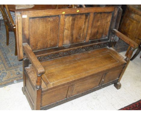 An early 20th Century oak monk's bench with folding top above a panelled front with blind fretwork carved frieze, on splayed 