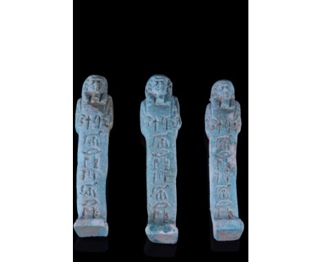 Late Period, 30th Dynasty, Ca. 332 BC.A group of three light blue faience ushabti figures, each wearing a tripartite wig, a f