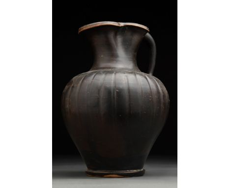 Ca. 400 BC.A black glazed pottery vessel with a globular rounded ribbed body swelling out from a low ring foot. The lip is pi