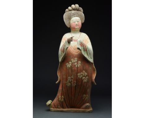 Ca. 618-907 AD.A ceramic 'Fat Lady' figure standing facing forward, with one foot angled to the side. She wears long-sleeved,