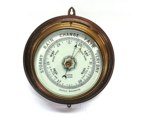 AN EARLY 20TH CENTURY ANEROID BAROMETER retailed by Gamage of London, the lacquered brass drum set to a circular dark oak bac