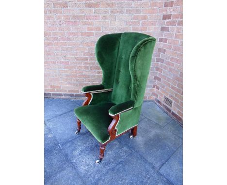 A LATE VICTORIAN WING ARMCHAIR  with carved mahogany frame on turned front supports with ceramic casters