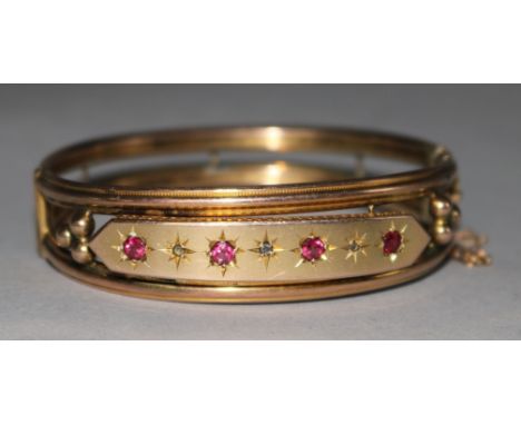 A late Victorian 9ct gold, ruby and diamond set hinged openwork bangle.