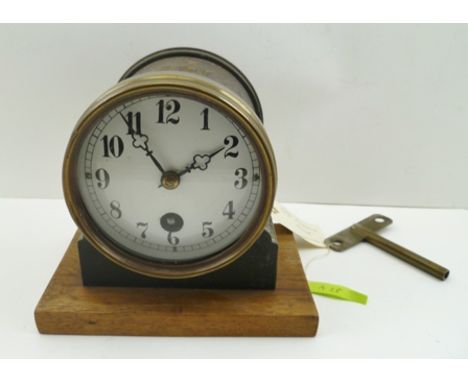 A MANTEL CLOCK, the movement set in a tin case with brass bezel, on an oak board base, white enamel dial with Roman numerals,