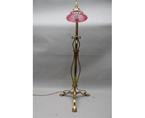 A DECORATIVE BRASS ADJUSTABLE STANDARD LAMP, having wrought decoration with flower head screws, on triform base, fitted with 