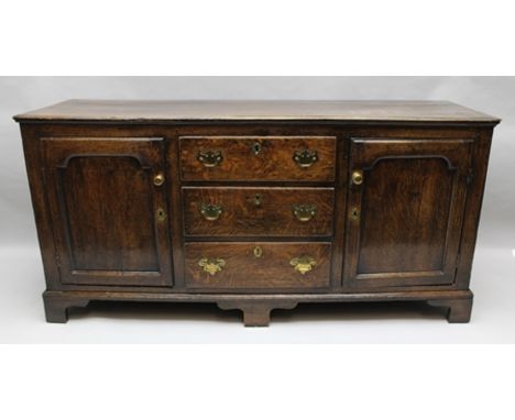 A GEORGE III OAK DRESSER BASE fitted three central drawers, flanked by panelled door cupboards, decorative brass handles, on 
