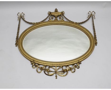 A REGENCY DESIGN WALL MIRROR, gilt framed with urn finial, flanked by bell husk and ribbon swags, to the base a tied ribbon a