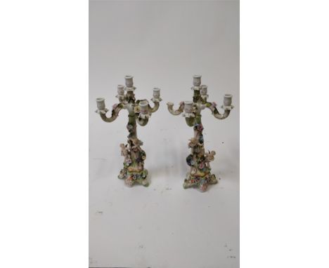 A pair of German ceramic five branch candelabras, each decorated with cherubs on the stem