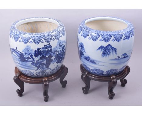 A PAIR OF JAPANESE BLUE AND WHITE PORCELAIN HIBACHIS on hardwood footed stands, each decorated with landscape scenes, hibachi