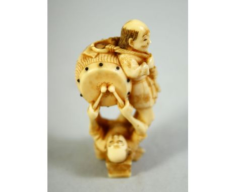 A JAPANESE CARVED IVORY NETSUKE, of a standing male figure with a drum upon his back, a figure beneath him with sticks, signe