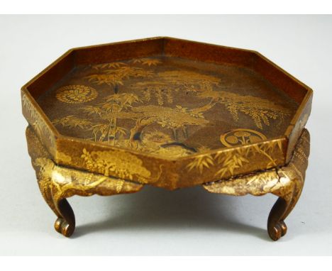 A JAPANESE GOLD LACQUER OCTAGONAL STAND, finely decorated with prunus trees, bamboo and bamboo on a hill, bearing two circula