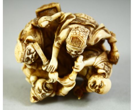 A JAPANESE CARVED IVORY NETSUKE, carved as four figures in a circle holding brushes, with red seal inset to base, 5cm wide.