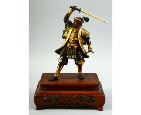 A JAPANESE GILDED BRONZE OKIMONO, of a samurai standing figure, his right arm held aloft holding a katana, mounted to a carve