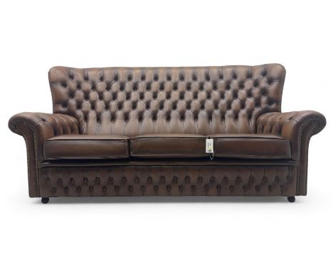 Three-seat hardwood-framed sofa, high wingback upholstered in buttoned brown leather, on castors Dimensions: Height:&nbsp;94c