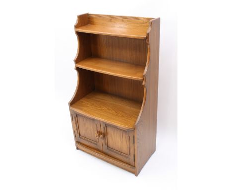 An Ercol Windsor elm waterfall bookcase - with Ercol label to reverse, with three graduated shelves over a two-door cupboard 