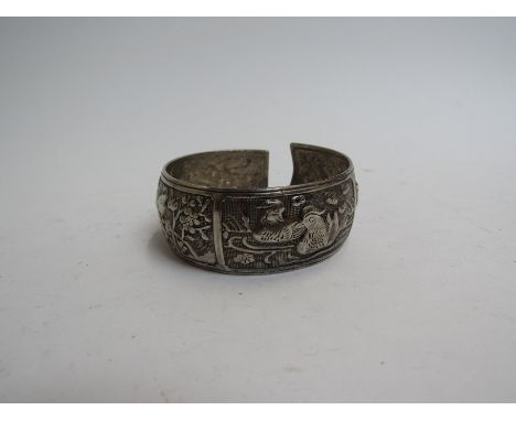 An Eastern embossed silver bangle with panels of birds and wild animals, 6cm diameter, 34g