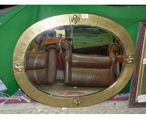 A wall mirror, oval shaped with textured brass frame having Fleur de lys detail and bevel edge, 32" x 24 3/4".