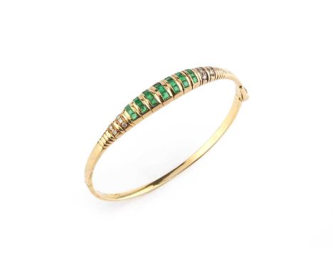 An emerald and diamond bangle, of hinged oval form, the tapered frontispiece with channels of square step-cut emeralds and ro