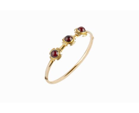 A Victorian garnet set bangle, of hinged oval hollow form, applied with a trio of foliate scroll decorated panels, each centr