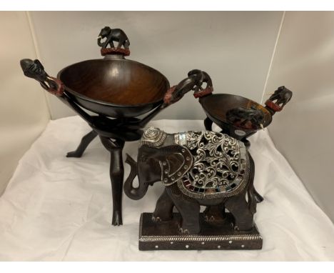 THREE ELEPHANT THEMED ITEMS TO INCLUDE TWO BOWLS ON TRIPOD LEGS AND A HIGHLY DECORATIVE WOODEN ELEPHANT ON PLINTH 