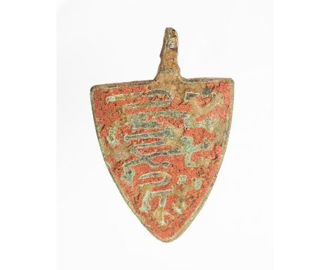 A complete cast copper-alloy and enamel harness pendant dating to the Medieval period, c. 1200-1400. The pendant is shield-sh