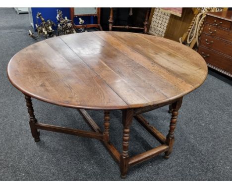 A large George III oak gate leg table, of oval design, on turned supports, united by a lower stretcher, on turned circular fe