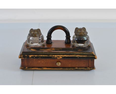 A stained wooden desk top inkwell, having two glass slot in wells with pussy cat head hinged metal lids, either side ebonised
